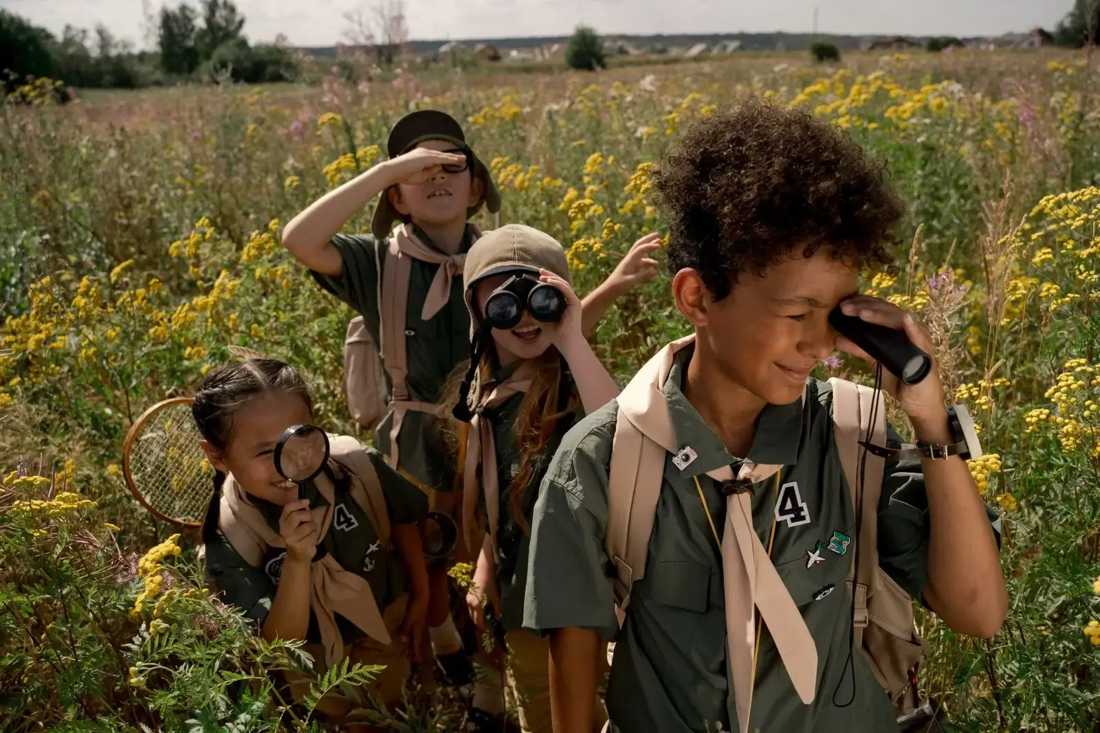A group of children in scout uniforms exploring a field with outdoor gear.
